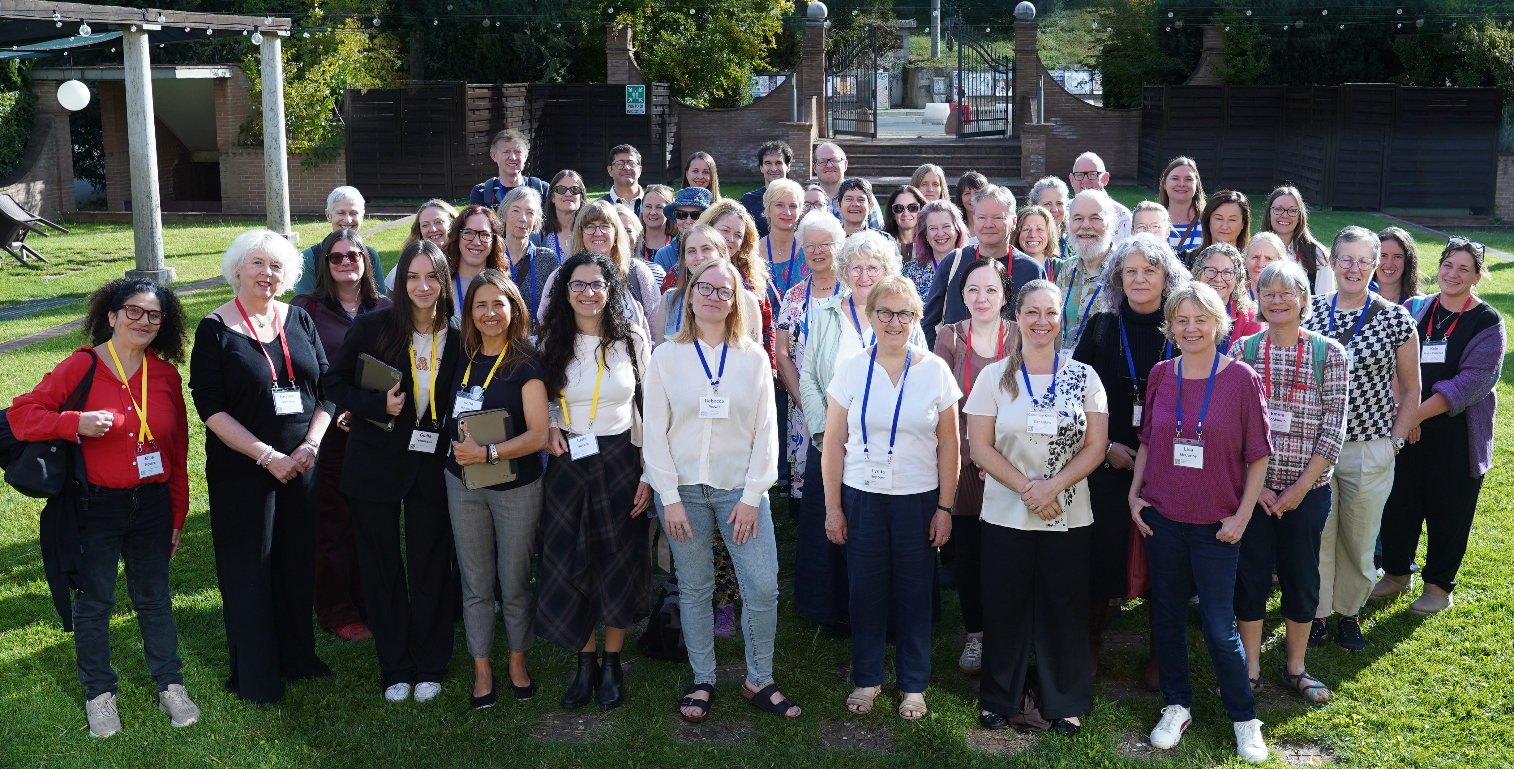 Photo of MET helpers taken at METM26. A large group of people stand on a grassy lawn with buildings in the background.